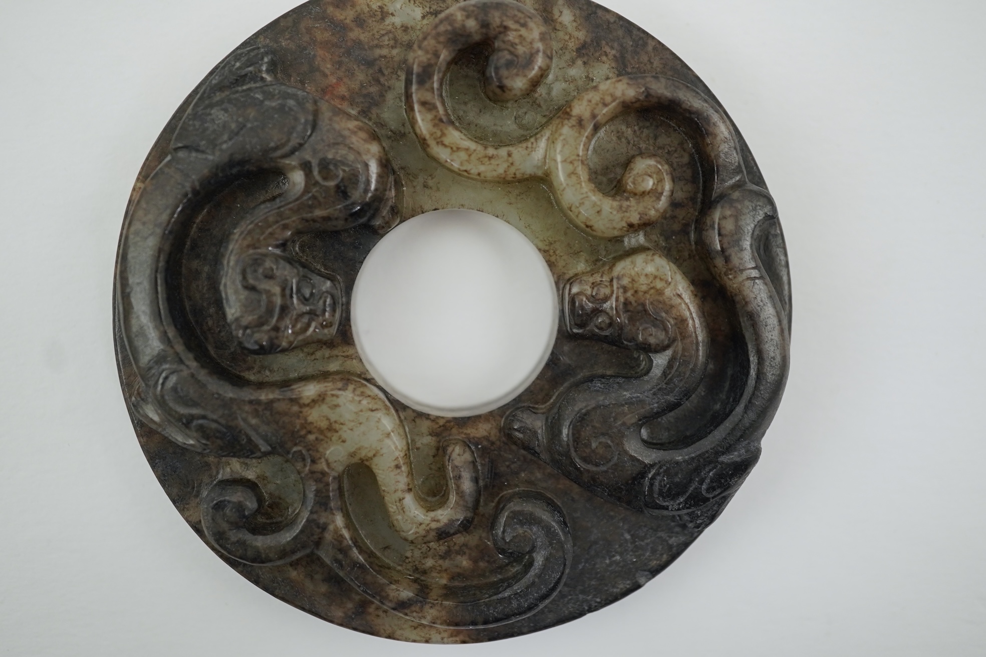 A Chinese pale celadon and black jade bi disc